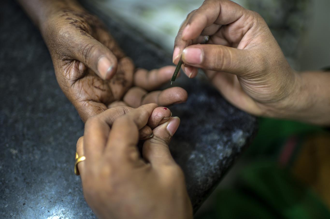One set of hands takes a small blood sample from someone's index finger